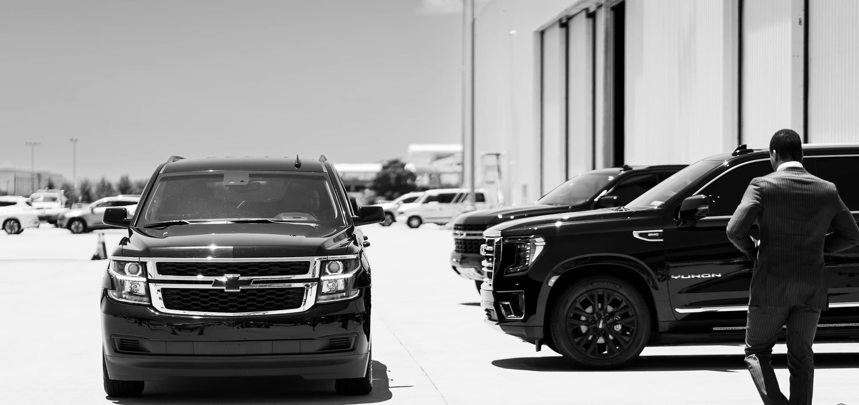 Airpros chauffeur greeting a client beside our fleet of black SUVs